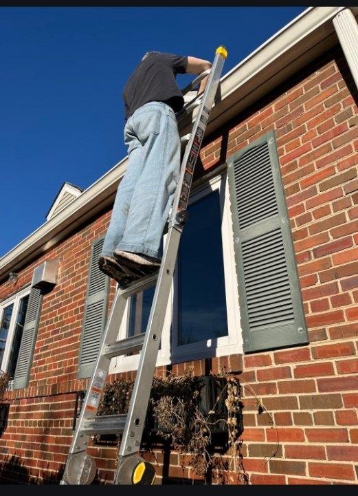 Phil cleaning exterior windows from a ladder on a brick home